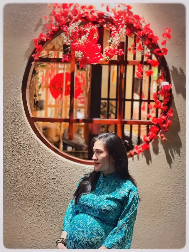 Bà bầu chụp ảnh cạnh khung cửa tròn kết hoa đỏ