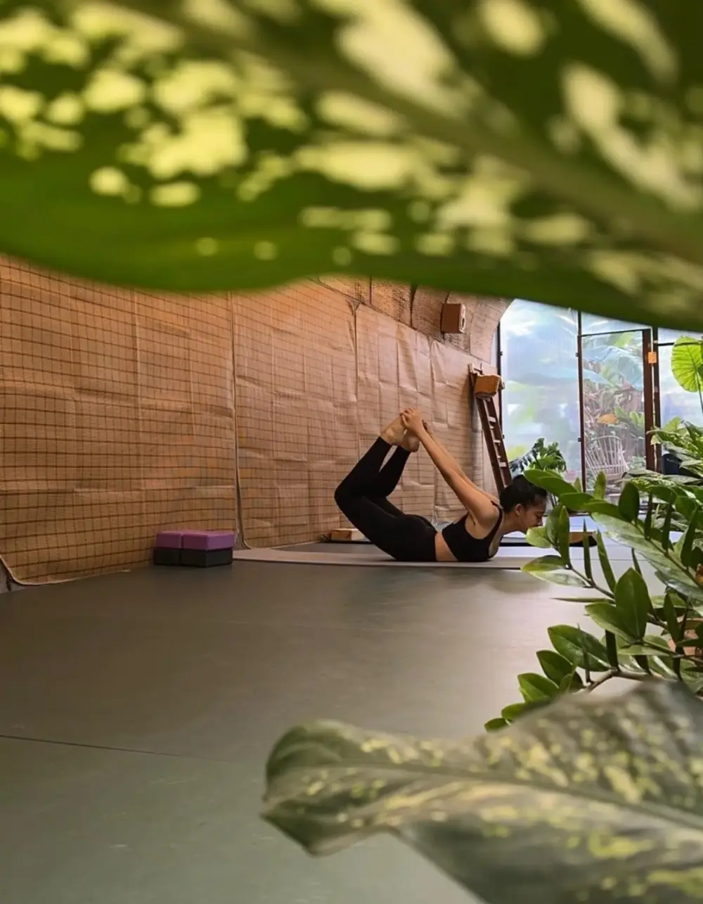 Một tư thế yoga bên tấm mành tre và lá cây
